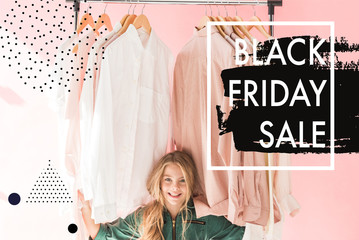 cheerful charming kid in trendy overalls sitting under clothes on hangers, black friday sale banner