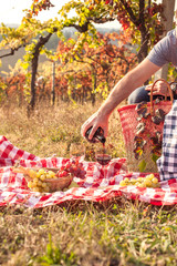 Wall Mural - Picnic at sunset in the hills of Italy. Vineyards and open nature in the fall. Romantic dinner, a man pours a glass of red wine. Free space for text. Copy space.