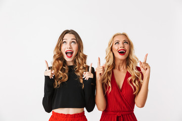 Emotional young two girls friends gossiping isolated over white wall dressed in black and red clothes pointing to copyspace.