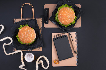 Wall Mural - Big hamburger, beer and notebook for planning on a black background. Fast food and snacks. Free space for text. Flat lay. Copy space.