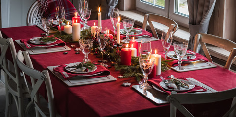 Table served for Christmas dinner, festive setting with decorations, burning candles and fir-tree branches