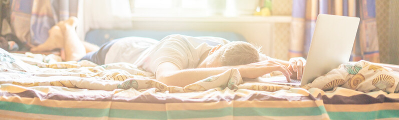 young person lying and sleeping on the bed in the sunny morning after working on laptop in the night f