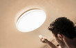 Man using remote control to set the simple big ceiling plafone lamps light intensity, electricity light control concept.