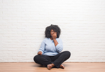 Poster - Young african american woman sitting on the floor at home looking stressed and nervous with hands on mouth biting nails. Anxiety problem.