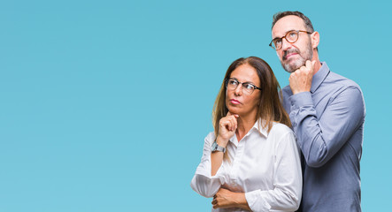 Wall Mural - Middle age hispanic couple in love wearing glasses over isolated background with hand on chin thinking about question, pensive expression. Smiling with thoughtful face. Doubt concept.