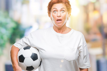 Sticker - Atrractive senior caucasian redhead woman holding soccer ball over isolated background scared in shock with a surprise face, afraid and excited with fear expression