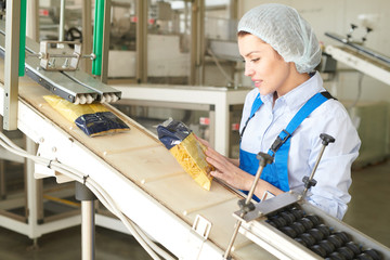 Wall Mural - Portrait of female factory worker controlling  packaging process at modern food factory and looking at macaroni bags sliding down conveyor belt, copy space