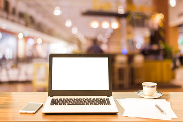 Wall Mural - Mockup image of laptop with blank white screen on wooden table blurred images In the coffee shop at shopping mall background.