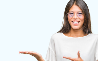 Young asian woman wearing glasses over isolated background amazed and smiling to the camera while presenting with hand and pointing with finger.