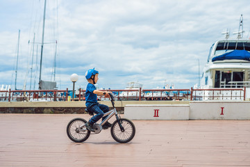 Wall Mural - Happy kid boy having fun near the yacht club with a bicycle on beautiful day. Active child wearing bike helmet