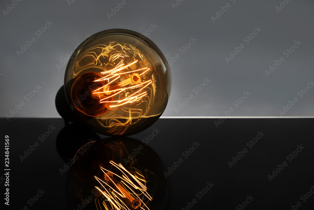 Glowing retro light bulb with reflection on dark table