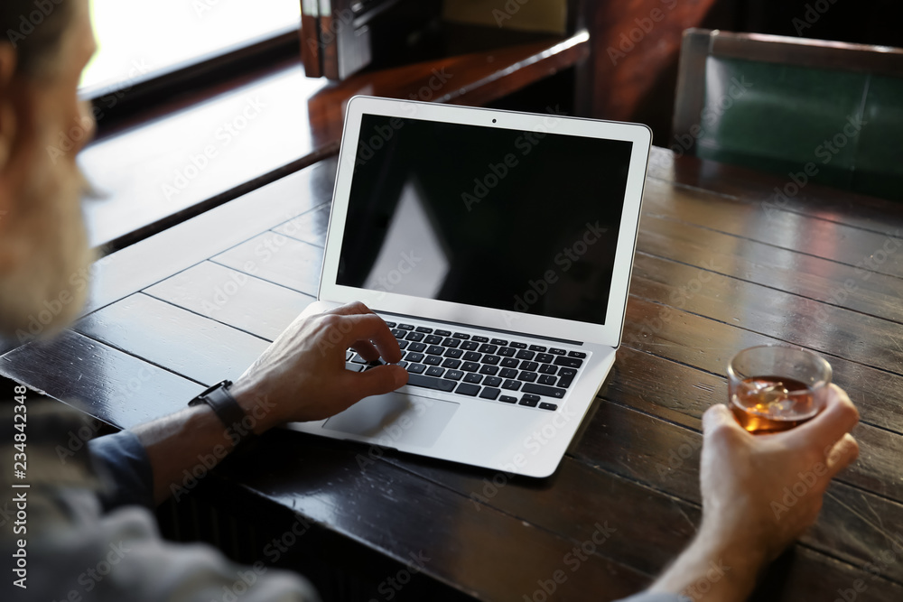 Senior man drinking whiskey while working on laptop in pub