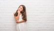 © Krakenimages.com - Young hispanic kid over white brick wall with hand on chin thinking about question, pensive expression. Smiling with thoughtful face. Doubt concept.