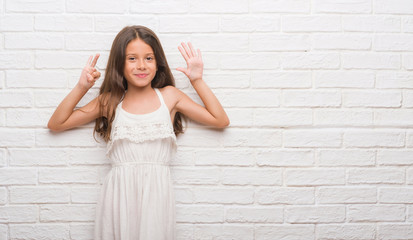 Wall Mural - Young hispanic kid over white brick wall showing and pointing up with fingers number seven while smiling confident and happy.