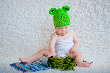 A child in a funny frog hat is playing with green grass