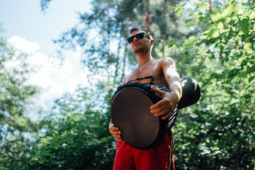 Wall Mural - guy in glasses and red shorts playing a djembe in woods