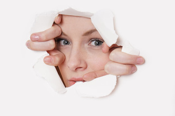 young woman peeking through hole in paper wall 