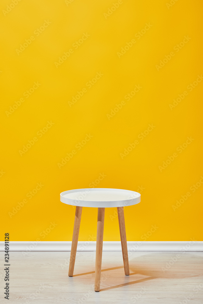 Minimalistic little wooden table near yellow wall - obrazy, fototapety, plakaty 
