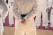 A trainer in a kimono stands with his back with his arms folded in the back in front of his students.