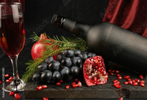 Fotografía Still-life with pomegranates, fir branches, black grape and bottle on the backgr
