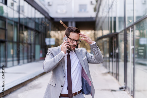 Fotografía Worried businessman dressed in formal wear using smart phone for a business talk while walking on the street
