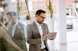 © BGStock72 - Happy businessman dressed in suit standing  in modern office  and using tablet