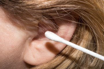 A woman cleans her ears with a cotton swab.Background man cleans ears.