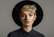  Fashion portrait of female model with blond short hair wear black hat and looking at camera