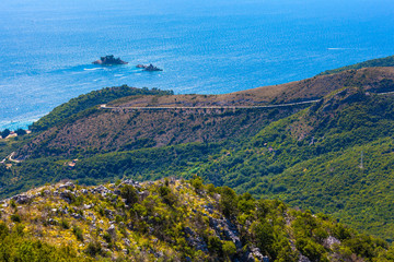  Serpentine - a winding mountain asphalt road in a dense green forest among the rocky slopes leading to the coast of Adriatic sea. Summer in the mountains of Montenegro.