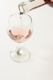 Fototapeta Paryż - Transparent glass of wine. Pink wine. Festive mood. Alcohol for a group of friends. Delicious drink. Light background. Noble drink. Lavender and rose wine. Wine from lavender