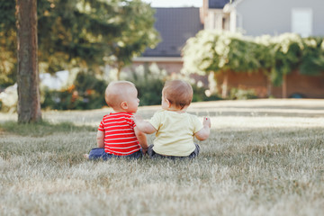 Two adorable little Caucasian babies sitting together in field meadow outside.View from back behind. Little happy children in summer park on sunset. Talking communication with friend concept