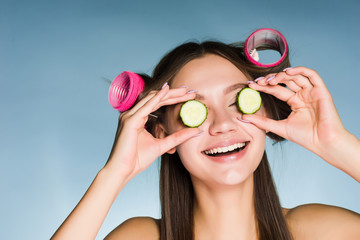 Poster - happy young girl going to a party, moisturizes the skin on her face with the help of cucumbers, on her hair curlers head