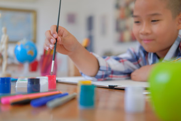 Wall Mural - asian kid boy child schoolboy holding paint brush drawing painting watercolor. children leisure activity at home