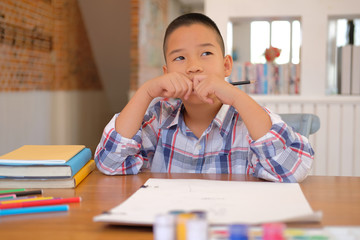 Wall Mural - asian kid boy child schoolboy thinking while drawing picture. children activity at home