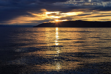 Sunset on Lake Baikal. Dark water and sky. Sun rays over the mountain