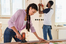 Selective Focus Of African American Woman Working With Jigsaw While Her Boyfriend Standing Behind During Renovation At Home
