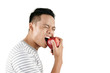 © DragonImages - Waist-up portrait of young Asian man wincing painfully while eating fresh red apple against white background, copy space