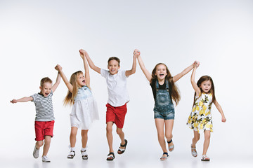 Wall Mural - Group of fashion cute preschooler kids friends running together and looking at camera on a white studio background. The friendship, fashion, summer concept. Space for text.