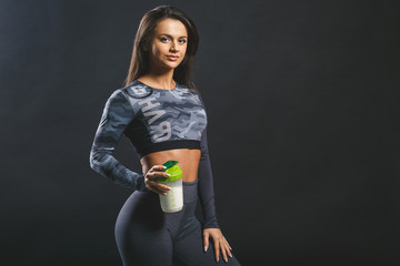 Wall Mural - Attractive young woman with protein shake bottle isolated over black background.