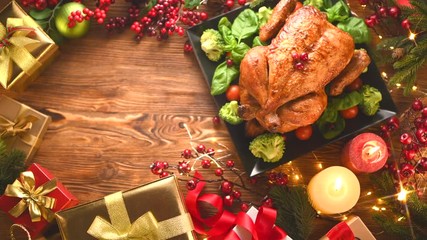 Wall Mural - Christmas dinner. Roasted chicken on holiday table, decorated with gift boxes, burning candles and garlands. Roasted turkey over wooden background. Top view, flatlay. 4K UHD video footage 3840X2160