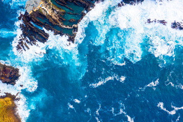 Aerial view of the ocean island cliffs with huge white waves and crystal blue water