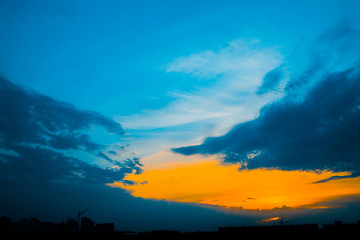 Wall Mural - atmospheric blue cloudy sky behind silhouettes of city buildings. cobalt and orange background of su