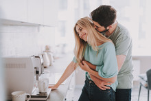 Bearded Guy Standing Behind Attractive Blonde Girl And Kissing Her. They Are Waiting For Hot Drink