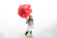 Portrait Of Smiling Girl Standing In A Lake Holding Oversized Red Artificial Flower