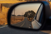 Looking In A Rear View Mirror While Driving Down A Country Road.