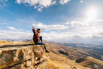 active young girl leads a healthy lifestyle, sits on the edge of the mountain and enjoys the sun and nature