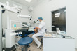 © ivandanru - Doctor used microscope. Dentist is treating patient in modern dental office. Operation is carried out using cofferdam. Client is inserted and restored teeth, make denture. Orthodontist and assistant