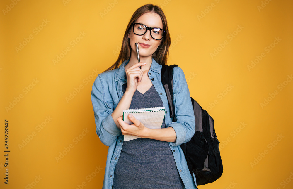 Happy and excited cute young student girl portrait in glasses with backpack isolated in studio - obrazy, fototapety, plakaty 
