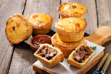 Wall Mural - Traditional Australian Mini meat pies from shortbread dough on a wooden board over wooden background.