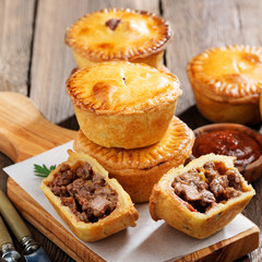 Wall Mural - Traditional Australian Mini meat pies from shortbread dough on a wooden board over wooden background.